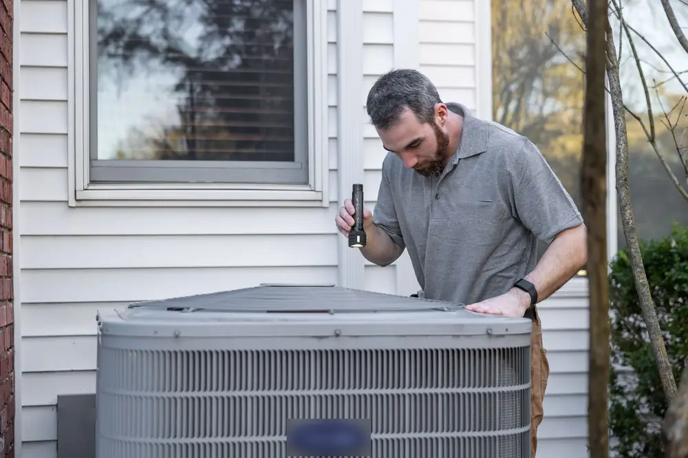 Technician inspecting an outdoor air conditioner with a flashlight